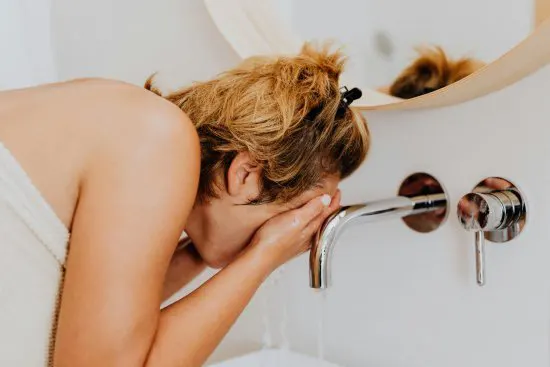 Donna che si lava il viso con acqua dura del rubinetto.