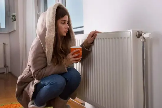 Ragazza con il cappotto appoggiata a un radiatore a causa di una caldaia che funziona male per il calcare.